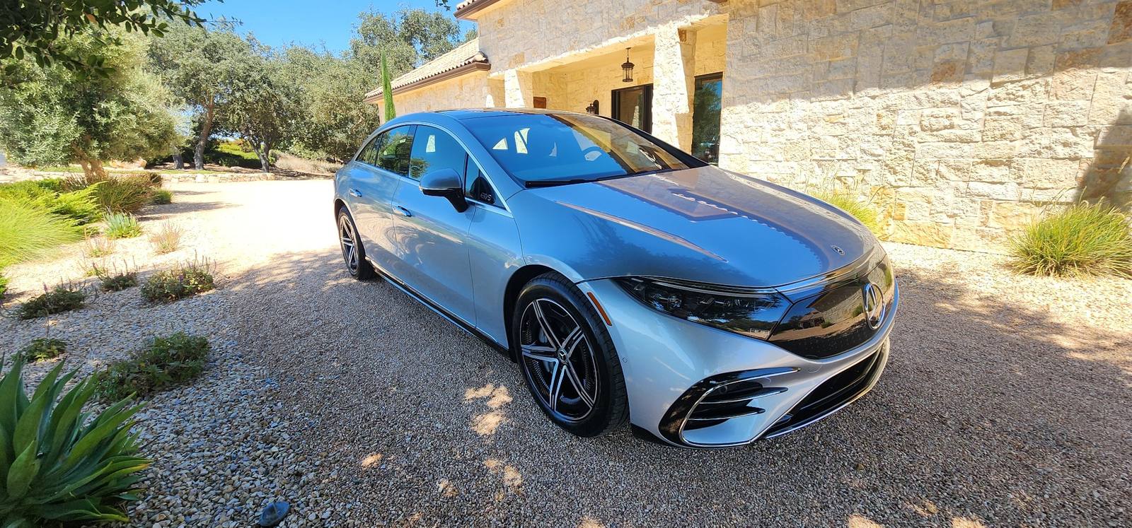 Silver Mercedes-Benz EQS luxury electric sedan detailed exterior at upscale home driveway